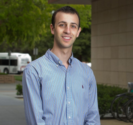 Photo of Dr. Adam de la Zerda in front of a beige-walled building with trees behind.