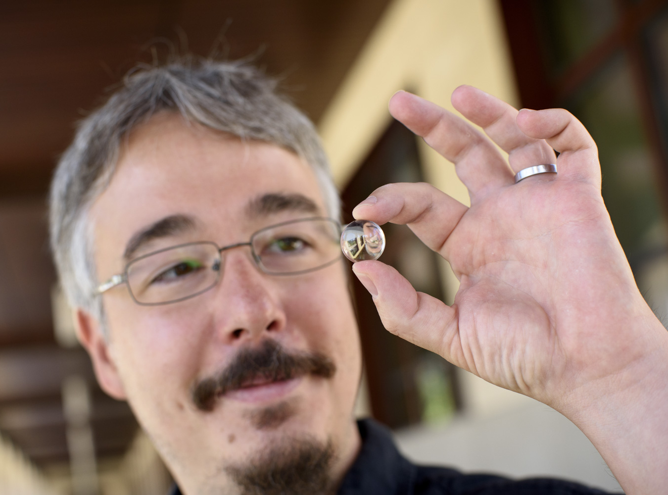 Man holding up small spherical lens, which looks like a glass ball, between thumb and forefinger.