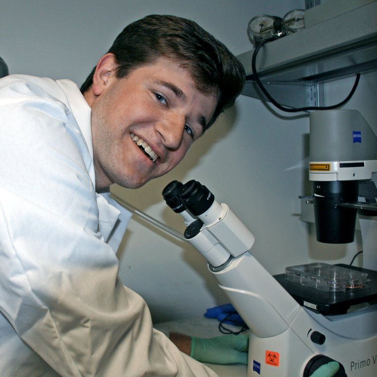 Photo of USRP student Carson Poltorack in the laboratory, looking through a large microscope.