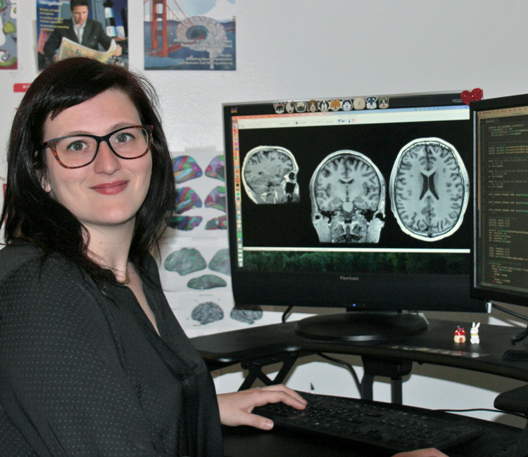 Photo of graduate student Corey Fernandez in a dry lab, working on a computer showing several brain scans.