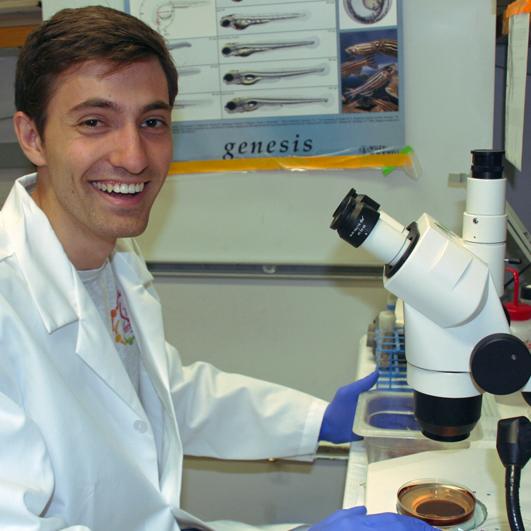 Photo of USRP student Scott Fleming in the lab, examining a dish of samples under a microscope.