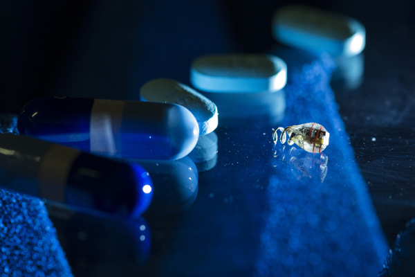photo by Austin Yee - a batteryless electrostimulator next to medicinal pills for size comparison. The new powering method allows the device to be wirelessly powered deep inside the body.