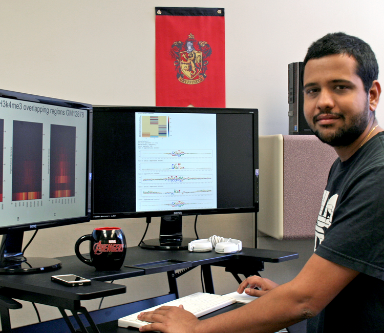 Photo of graduate student Lawrence Bai in a dry lab, working on a computer showing colorful graphs and DNA data.