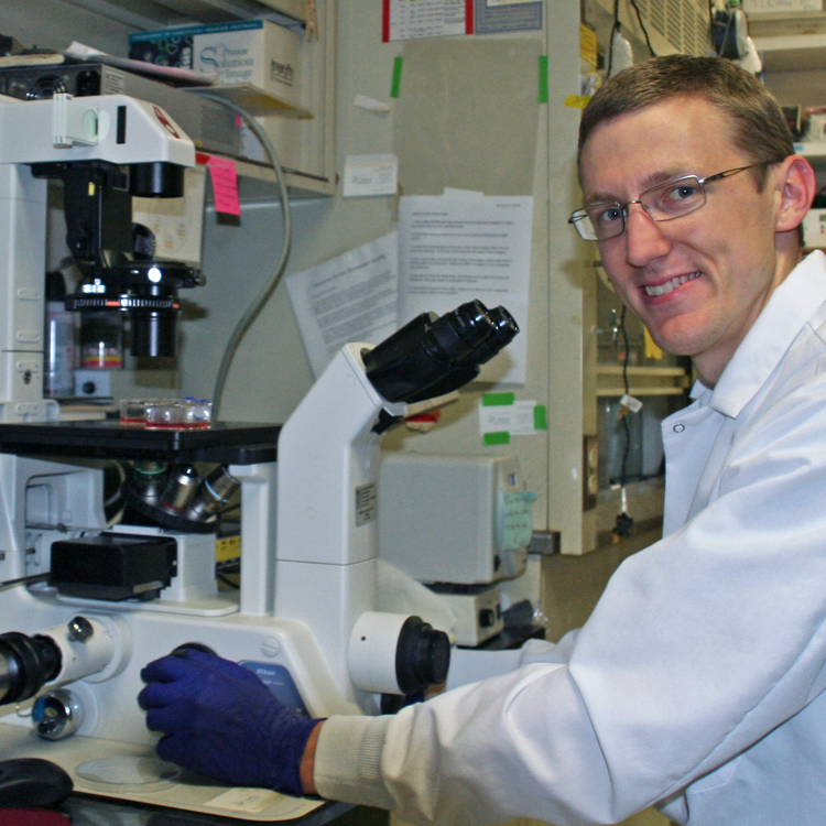 Photo of graduate student Terence Theisen in the lab, operating a large microscope system.