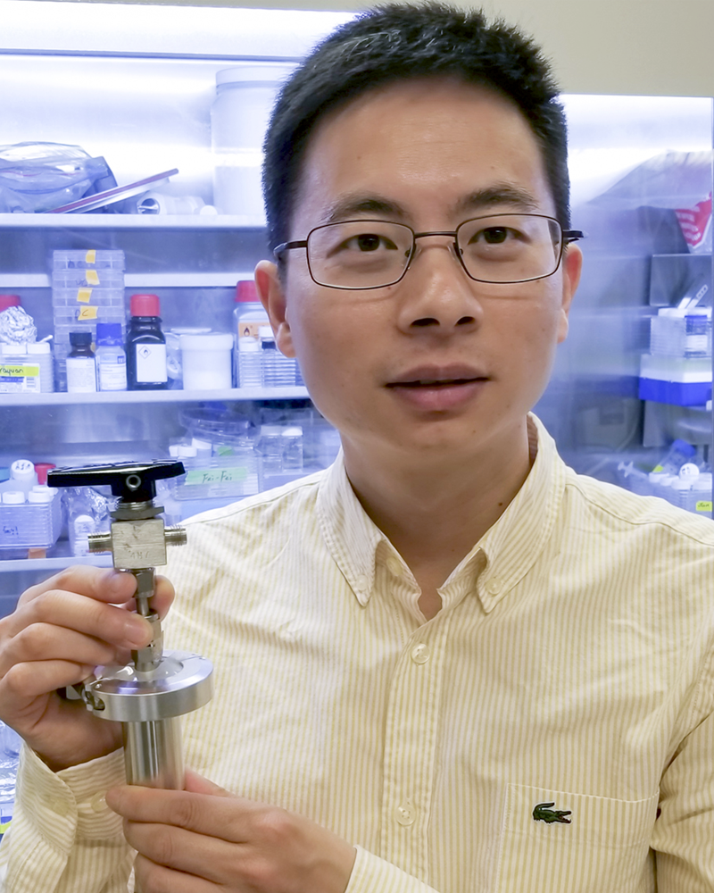 Photo of young Asian man holding up a silver device.