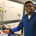 Indoor photo of a graduate student standing next to tissue culture hood.