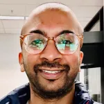 Indoor headshot photo of a smiling man with glasses and a beard.