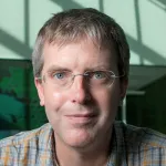 Photo of a smiling white male faculty member with short brownish-gray hair and glasses, Dr. Drew Endy, Associate Professor of Bioengineering at Stanford University.