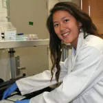Indoor photo of a graduate student workign with a cell plate near equipment.