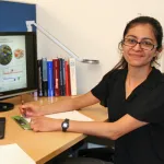 Indoor photo of a graduate student sitting next to a computer, writing notes.