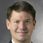 Photo of smiling white male faculty member with short brown hair, Dr. Joel Neal, Associate Professor of Medicine at Stanford University.