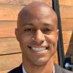 Outdoor headshot photo of a smiling Black male faculty member, Dr. Kyle Daniels, Assistant Professor of Genetics at Stanford University.