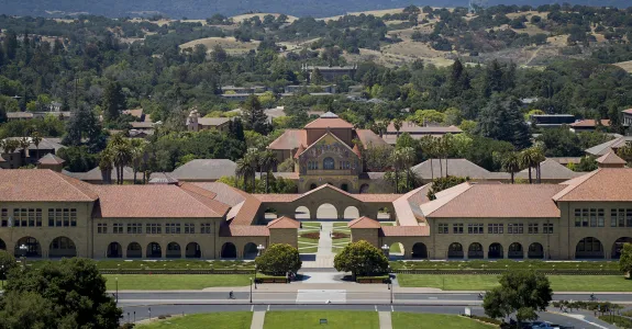 Outdoor overhead photo of Stanford campus, focused on the entrance to the main quad with the Memorial Church facade visible, with the foothills in the background.