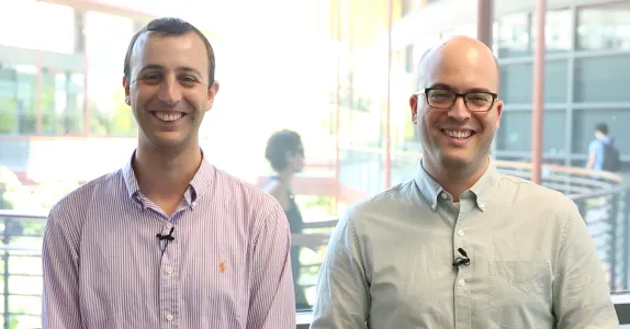 Indoor photo of Dr. Adam de la Zerda and Dr. Yonatan Winetraub, two adult white male faculty members at Stanford, standing side by side and smiling at the camera, one wearing glasses.