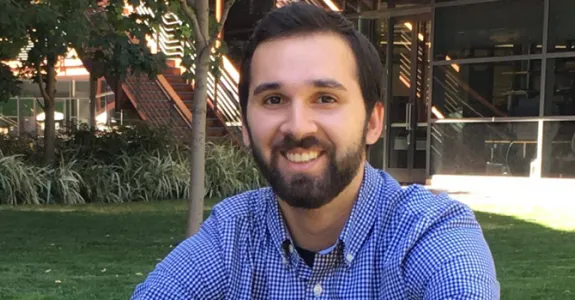 Photo of bearded young man sitting on the lawn at the James H. Clark Center.