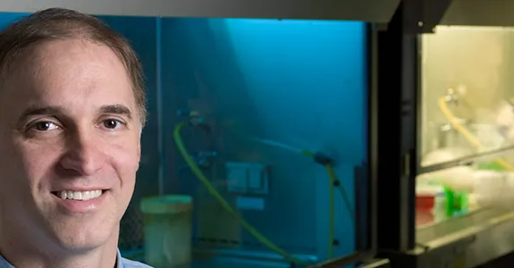 Photo of Dr. Steven Artandi in the lab, with a student working in a fume hood in the background.