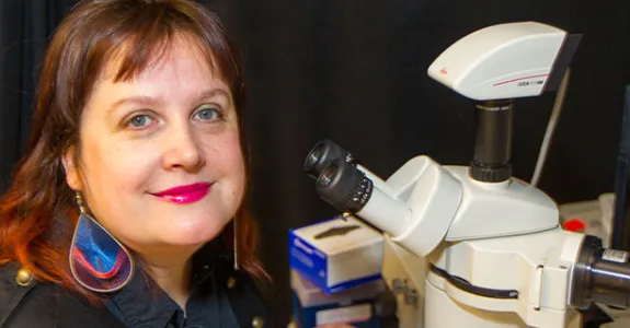 Photo of Dr. Maria Barna in the lab next to a microscope.