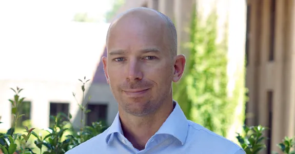 Photo of Dr. Ben Domingue in front of trees and a building.
