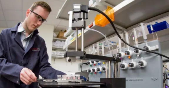 Photo of undergraduate student Zachary Rosenthal loading protein samples onto the crystallization robot at Macromolecular Structure Knowledge Center.