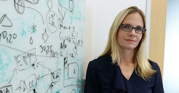 Photo of faculty member Christina Curtis standing in front of a whiteboard covered in notes.
