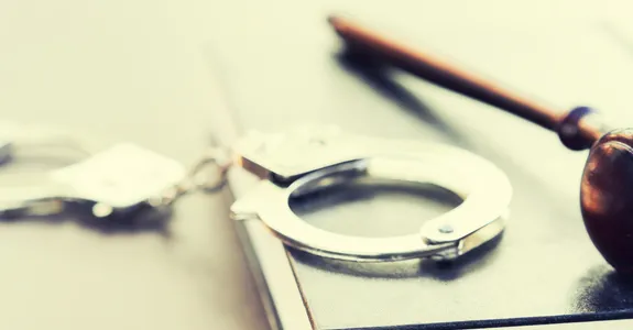 Photo of a gavel on top of a law book with a pair of handcuffs beside it.