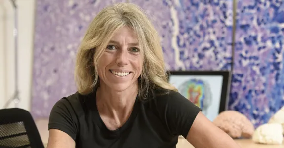 Photo of blonde female PI sitting at a table, with models of brains behind her.