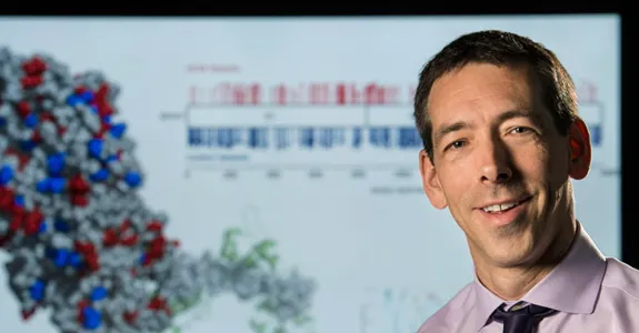 Photo of Dr. Euan Ashley in front of a screen showing a 3D image of a molecule.