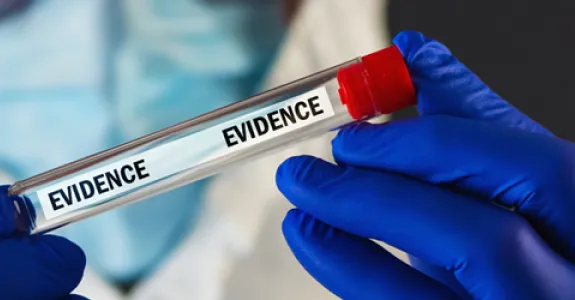 Photo of a man in hazard safety gear wearing blue gloves and holding up a vial labeled "evidence".