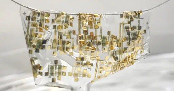 Photo showing the extremely flexible semiconductor draped liquid-like over a human hair, with gold sensors dispersed throughout transparent semiconductor material.