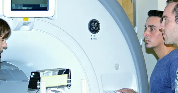 Photo of Professor Kalanit Grill-Spector, research associate Kevin Weiner, and graduate student Jesse Gomez next to MRI machine.