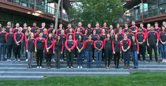 Photo of dozens of Stanford Bio-X PhD Fellows standing together in matching dark gray and red shirts.