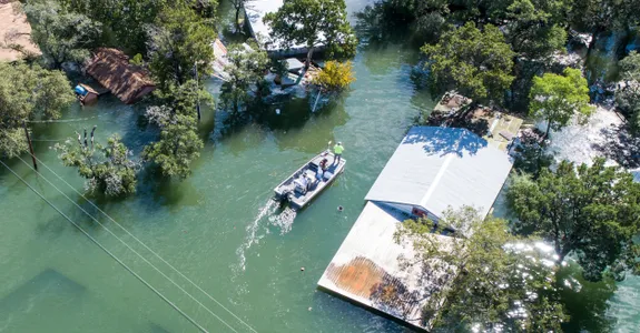 Photo showing a small motorboat with a few people inside moving around houses and trees almost entirely submerged by flooding.