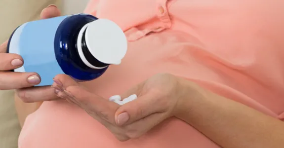 Photo of pregnant woman holding medicine bottle.