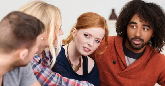 Photo of four diverse young people sitting together in a bedroom.