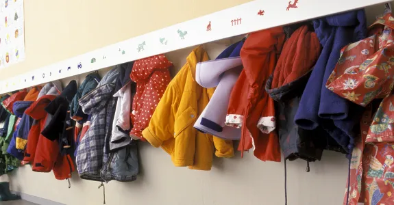 Photo of colorful children’s coats hung up on a wall rack.