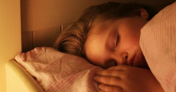 Photo of little girl sleeping in a bed with her hand beside her pillow.
