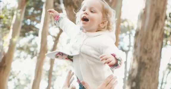 Photo of a man tossing his blonde toddler daughter in the air.