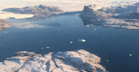 Large body of water in Greenland, broken by islands, with snowmelt visible.