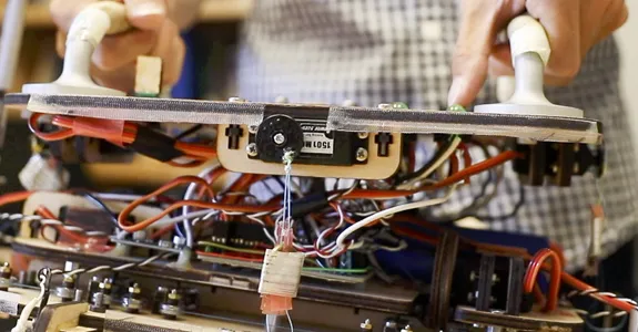 Student lifting up the robotic gripper by two handles, showing its interior wires.