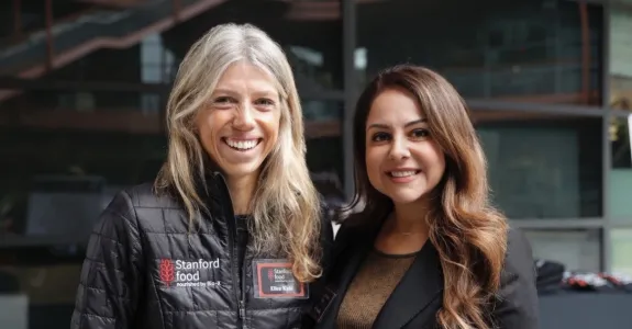 Photo of two women standing together outdoors, smiling at the camera.