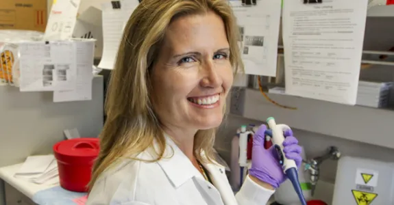 Photo of blonde female PI sitting at bench, using a pipette and smiling.