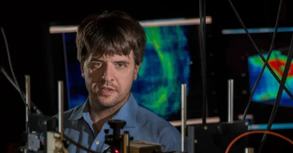 Photo of Dr. Karl Deisseroth in the laboratory, surrounded by equipment with wires and screens displaying brightly-colored optogenetic displays.