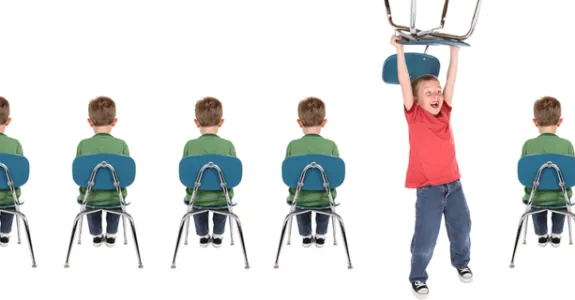 Photo of line of children sitting in chairs, with one child acting out.