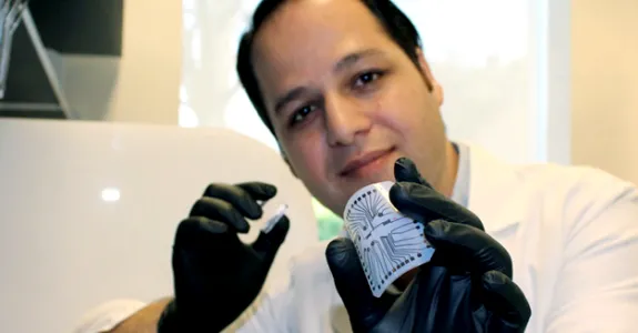 Photo of engineering research associate Rahim Esfandyarpour holding up and flexing small lab on chip device.