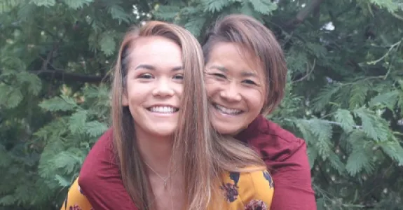 Photo of an Asian woman with her arms wrapped around her daughter from behind.