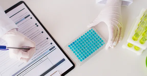 Photo of scientist taking notes on clipboard next to test tubes.