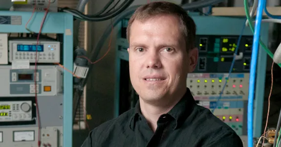 Photo of Dr. Nicholas Melosh in front of large pieces of equipment and several large wires.