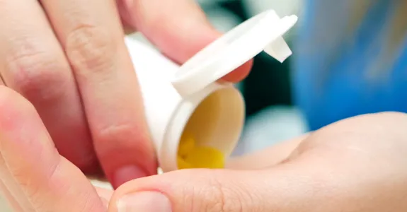 Photo of a woman's hands, pouring pills out of a bottle.