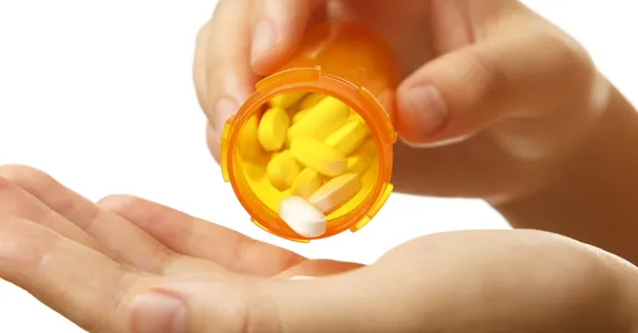 Photo of woman's hands pouring white pills out of a medication bottle into her palm.
