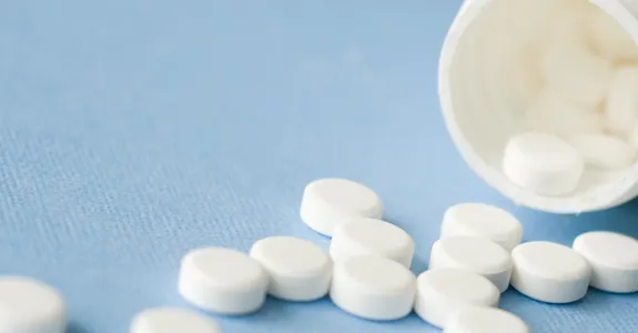 Photo of white bottle spilling white pills across a blue surface.